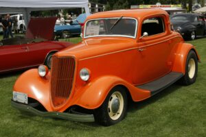 Bright orange vintage car showcased at an outdoor classic car exhibition.