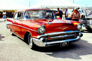 A vintage red 1957 Chevrolet showcased at an outdoor car exhibition with attendees.